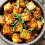 - Firm tofu and its preparation Use 14 oz of firm tofu. Press it for at least 15 minutes. This helps remove extra moisture. Next, cut the tofu into 1-inch cubes. This size helps with even cooking. - Cornstarch and seasonings You will need 2 tablespoons of cornstarch. This gives the tofu a nice crunch. Add 1 teaspoon each of garlic powder and onion powder. Season with salt and pepper to taste. Toss the cubed tofu in this mix until each piece is well coated. - Sweet chili sauce and garnishes Use ½ cup of sweet chili sauce for a tasty glaze. Add 1 tablespoon of soy sauce and 1 tablespoon of rice vinegar. This adds depth to the flavor. For garnish, slice 1 green onion and sprinkle sesame seeds on top. These add color and texture to your dish. First, you need to press the tofu. This removes extra moisture. Wrap the tofu in a clean towel. Place a heavy object on top for about 15 minutes. Once pressed, cut the tofu into 1-inch cubes. Next, it's time to coat the tofu. In a large bowl, mix together the cornstarch, garlic powder, onion powder, salt, and pepper. Toss the tofu cubes in this dry mix. Make sure each piece is coated evenly. This coating helps create a crispy texture. Drizzle 1 tablespoon of olive oil over the tofu. Gently toss it again to coat. This step is key for crispiness in the air fryer. Now, preheat your air fryer to 375°F (190°C). This takes about 5 minutes. While it heats, place the coated tofu cubes in the air fryer basket. Make sure they are in a single layer and not crowded. Air fry the tofu for 15-20 minutes. Halfway through, shake the basket. This helps the tofu cook evenly. Keep an eye on it until it's golden brown and crispy. While the tofu cooks, let’s make the sweet chili glaze. You will need: - ½ cup sweet chili sauce - 1 tablespoon soy sauce - 1 tablespoon rice vinegar In a small saucepan, combine these ingredients over medium heat. Stir often until everything is well mixed and heated through. This should take about 3-4 minutes. Once the tofu is crispy, transfer it to a large mixing bowl. Pour the sweet chili glaze over it. Gently toss to coat each piece. Now, your crispy tofu is ready to serve. Enjoy it hot, garnished with sliced green onions and sesame seeds! To get crispy tofu, start by pressing it. Pressing takes out extra water. This step makes the tofu firm and helps it brown well. Use a clean towel and a heavy pan to press it for at least 15 minutes. Next, cornstarch is your best friend. It coats the tofu and forms a crunchy layer. Mix cornstarch, garlic powder, onion powder, salt, and pepper in a bowl. Toss the pressed tofu cubes in this mix. Adding olive oil is also key. It helps the cornstarch stick and adds flavor. Drizzle one tablespoon over the coated tofu. Toss it again to coat all sides evenly. This preparation is crucial for that perfect crispy bite. To boost the flavor, think about adding more spices. You might try smoked paprika for a smoky taste or a pinch of cayenne for heat. These spices are easy to mix in with your cornstarch. When serving, make it fun! Pair your crispy tofu with rice or noodles. You can also add fresh veggies, like bell peppers or snap peas, for crunch. Top it with sliced green onions and sesame seeds. This adds a nice pop of color and texture to your dish. {{image_2}} You can switch up the sweet chili sauce for a spicy kick. Try adding sriracha or gochujang. These sauces add heat and flavor. For a tangy option, mix in lime juice or rice vinegar. This gives your dish a bright taste. If you need a vegan sauce, use coconut aminos instead of soy sauce. It has a milder flavor. You could also try a homemade mango salsa. This will add sweetness and texture to your dish. You can easily add vegetables for more color and flavor. Bell peppers, broccoli, or snap peas work well. Toss them in with the tofu before air frying. This helps them cook and get crispy too. Serving your crispy tofu over rice or noodles is a great idea. Jasmine rice or soba noodles pair nicely. You can also add a side salad for freshness. This makes your meal balanced and delicious. To store leftover crispy tofu, place it in an airtight container. Let it cool for about 30 minutes before sealing. Store it in the fridge for up to three days. To reheat, simply place it back in the air fryer for a few minutes. This helps keep the tofu crispy. If you want to freeze your crispy tofu, let it cool first. Place it in a freezer-safe bag or container. Make sure to remove as much air as possible to prevent freezer burn. It can stay good for up to three months. To use it, thaw it overnight in the fridge. Reheat in the air fryer for a quick and tasty meal. Yes, you can use extra-firm tofu. It has less moisture than firm tofu. This means it can be crispier when cooked. Press it for a shorter time if you choose extra-firm. The cooking method stays the same. Just make sure to coat it well with cornstarch for that perfect crunch. To make your tofu crispier, follow these tips: - Press Longer: Press the tofu for 30 minutes instead of just 15. This removes more moisture. - Use More Cornstarch: Try using 3 tablespoons of cornstarch for a thicker coating. - Air Fryer Temperature: Increase the air fryer temperature to 400°F (200°C). This will help it crisp up faster. - Don’t Overcrowd: Cook in batches if needed. This ensures hot air can reach all pieces. Yes, you can bake the tofu. Preheat your oven to 400°F (200°C). Place the coated tofu on a baking sheet lined with parchment paper. Bake for 25-30 minutes, flipping halfway through. The tofu will be crispy but may not be as crunchy as when using the air fryer. Use a broiler for the last few minutes for extra crispiness. This guide covers making crispy tofu, from ingredient prep to cooking. You learned how to prepare tofu, air fry it, and create a tasty sweet chili sauce. I shared tips for achieving that perfect crunch and suggested flavors to enhance your dish. Finally, I included storage methods and variations to keep things fresh. Enjoy experimenting with different sauces and vegetables. With these steps, you're ready to impress with your crispy tofu creations!