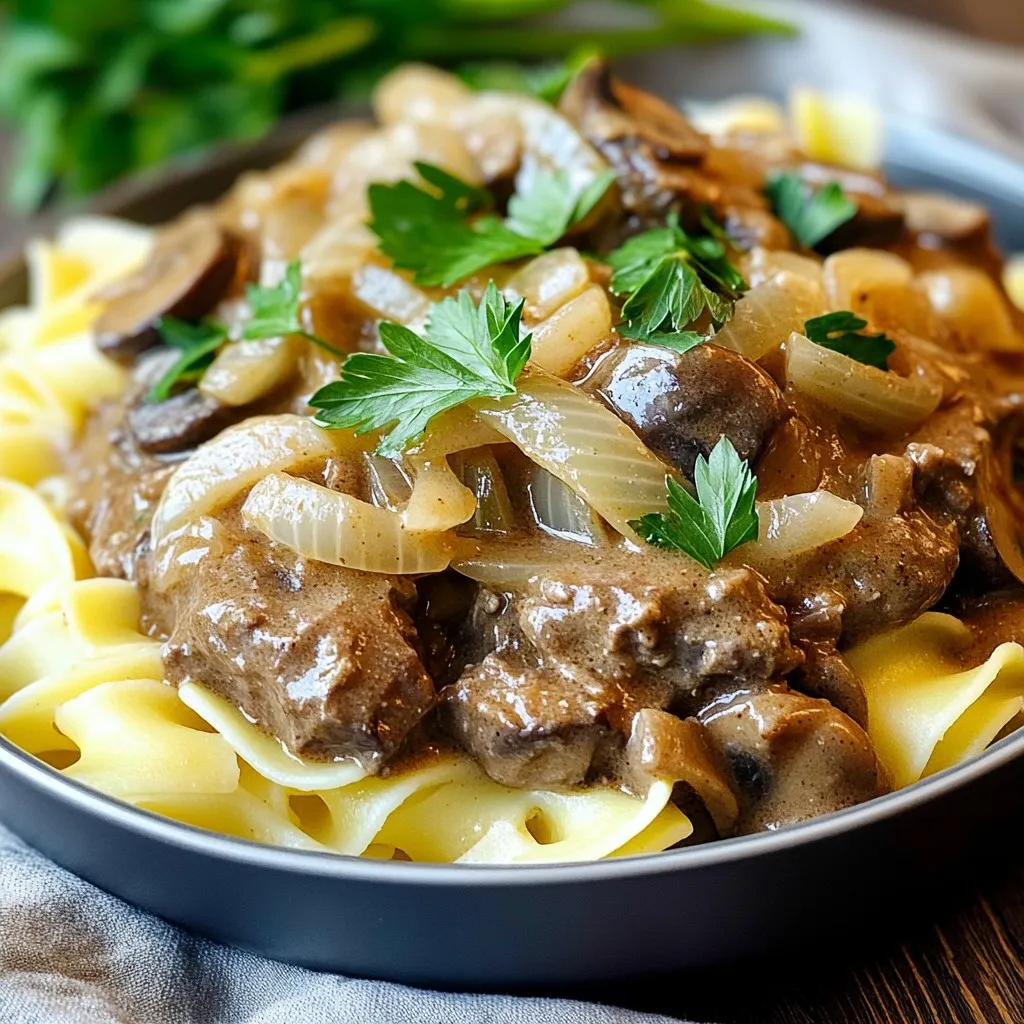 - 1.5 lbs beef stew meat, cut into bite-sized pieces - 1 medium onion, diced - 2 cloves garlic, minced - 8 oz mushrooms, sliced (button or cremini) - 1 cup beef broth - 1 tablespoon Worcestershire sauce (non-alcoholic) - 2 teaspoons Dijon mustard - 1 teaspoon dried thyme - 1 teaspoon paprika - Salt and pepper to taste - 1 cup sour cream - 3 tablespoons all-purpose flour - 1 tablespoon olive oil - Fresh parsley, chopped (for garnish) - Egg noodles or rice (for serving) - If you want to swap proteins, use chicken or tofu. Both work well. - For a vegan or vegetarian dish, replace beef with mushrooms and use vegetable broth. - You can also try chicken broth or mushroom broth for different flavors. - A slow cooker is essential for this recipe. It makes cooking easy. - Use a skillet for sautéing the onions, garlic, and mushrooms. - Mixing bowls are helpful for combining sauces and thickening agents. Every item on this list helps build the rich flavor and creamy texture of this dish. Enjoy making it! 1. Sautéing the onions, garlic, and mushrooms In a large skillet, I heat 1 tablespoon of olive oil over medium-high heat. I add 1 medium diced onion and cook for about 3-4 minutes until soft. Then, I stir in 2 minced garlic cloves and 8 ounces of sliced mushrooms. I keep stirring until the mushrooms turn brown, which takes about 5-6 minutes. This step brings out rich flavors. 2. Combining ingredients in the slow cooker Next, I take the cooked onion, garlic, and mushrooms and place them in the slow cooker. Then, I add 1.5 pounds of beef stew meat, cut into bite-sized pieces. In a bowl, I mix 1 cup of beef broth, 1 tablespoon of Worcestershire sauce, 2 teaspoons of Dijon mustard, 1 teaspoon of dried thyme, 1 teaspoon of paprika, and some salt and pepper. I pour this mixture over the beef and veggies in the slow cooker. 1. Setting the slow cooker (Low vs High) I cover the slow cooker and set it to cook. I can choose to cook it on low for 6-8 hours or on high for 3-4 hours. Cooking it on low gives the beef more time to become tender. 2. Timing for tender beef I check the beef after the cooking time. It should be tender and easy to pull apart with a fork. If it is not tender yet, I let it cook a little longer. 1. Thickening the stroganoff with sour cream About 30 minutes before I plan to serve, I mix 3 tablespoons of flour with 1 cup of sour cream in a small bowl until smooth. I then stir this mixture into the stroganoff in the slow cooker. This will help thicken the sauce. 2. Serving suggestions I serve the stroganoff over cooked egg noodles or rice. A sprinkle of fresh chopped parsley on top adds a nice touch. This dish looks as good as it tastes! To get the best beef stroganoff, follow these tips: - Preventing overcooking: Use the low setting for tender meat. High heat can dry out beef. Check your slow cooker’s heat. Each brand may cook differently. - Checking for doneness: The beef should be fork-tender when it's done. If it’s tough, let it cook longer. Always test before serving. Boost the taste of your stroganoff with these ideas: - Adding spices or herbs: Try adding more thyme or a bay leaf for depth. A pinch of red pepper flakes can add some heat. Fresh herbs, like parsley, are great too. - Recommended side dishes: Serve over egg noodles or rice for a classic touch. A side of steamed veggies or a fresh salad pairs well too. Avoid these typical errors to ensure a perfect dish: - Ingredient mishaps: Make sure you have all ingredients ready. Forgetting the Worcestershire sauce or flour can change the taste and texture. - Timing issues: Don’t rush cooking time. If you cut it short, the beef may not be tender. Stick to the cooking times for the best results. {{image_2}} You can change the mushrooms in this dish. Try using shiitake or portobello for a deeper flavor. Each type brings its own taste and texture. If you want something different, swap the beef for chicken or tofu. Chicken gives a lighter taste, while tofu adds protein without meat. For a gluten-free meal, use cornstarch instead of flour. It thickens the sauce just as well. You can also use gluten-free noodles or rice to serve. If you need a dairy-free option, try coconut cream. It makes a rich sauce without dairy. Add a little red wine to the broth for a richer taste. It deepens the flavor and adds complexity. For a spicy kick, mix in some crushed red pepper flakes. This will warm up the dish and give it a fun twist. Enjoy trying these new ideas! After enjoying this tasty beef and mushroom stroganoff, let it cool down. Place leftovers in a clean, airtight container. Store in the fridge for up to three days. For longer storage, you can freeze it. Use freezer-safe bags or containers. Make sure to remove as much air as possible. This helps prevent freezer burn. The stroganoff will last up to three months in the freezer. Reheating is simple and quick. The best method is using the stove. Just place the stroganoff in a pan. Heat it on low, stirring often. This helps keep the sauce creamy. You can also use a microwave. Heat in short bursts of one minute. Stir in between to avoid hot spots. Be careful not to overcook it. This can make the sauce too thin or dry. You can store beef stroganoff in the fridge for three days. If frozen, it can last up to three months. Check for signs of spoilage before eating. If it smells off or has a strange color, it's best to toss it. Always trust your nose and eyes. Keeping food safe is important for your health. Yes, you can use frozen beef stew meat. To thaw it, place the meat in the fridge overnight. If you need it quickly, use the microwave on the defrost setting. Once thawed, you can brown it in the skillet as usual. This step adds great flavor. Be sure to increase the cooking time by about an hour when using frozen meat in your slow cooker. You can prep this dish ahead of time easily. Start by chopping the onions and mushrooms. Store them in the fridge until you're ready to cook. You can also mix the broth, Worcestershire sauce, and seasonings in a bowl. Keep this mixture in the fridge. On the day you want to cook, just combine all the ingredients in the slow cooker and set it to cook. Beef stroganoff pairs well with many sides. Here are some favorites: - Egg noodles - Rice - Mashed potatoes - Steamed vegetables - Fresh salad These options will make your meal complete and delicious. This blog post covered all aspects of making a delicious beef stroganoff. We reviewed the ingredients needed, including beef, vegetables, and various seasonings. I shared tips for proper cooking and mistakes to avoid. The variations allow you to customize the dish for different diets and tastes. In closing, mastering beef stroganoff is all about using the right tools and techniques. Enjoy experimenting with flavors and variations to make it your own. Your cooking will impress every time.